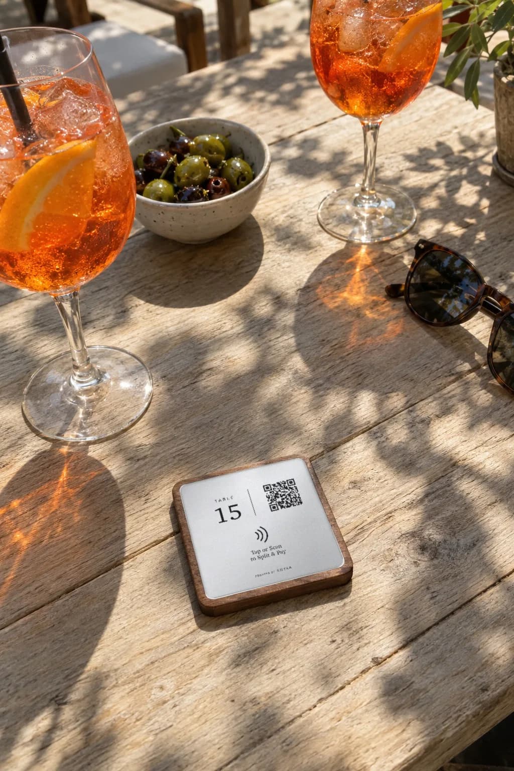 A RHYKA plaque for table 15 lying on a sunny patio table between two spritzes