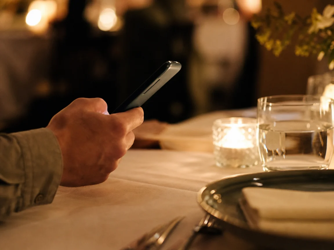 A guest holding a phone above a warmly lit restaurant table